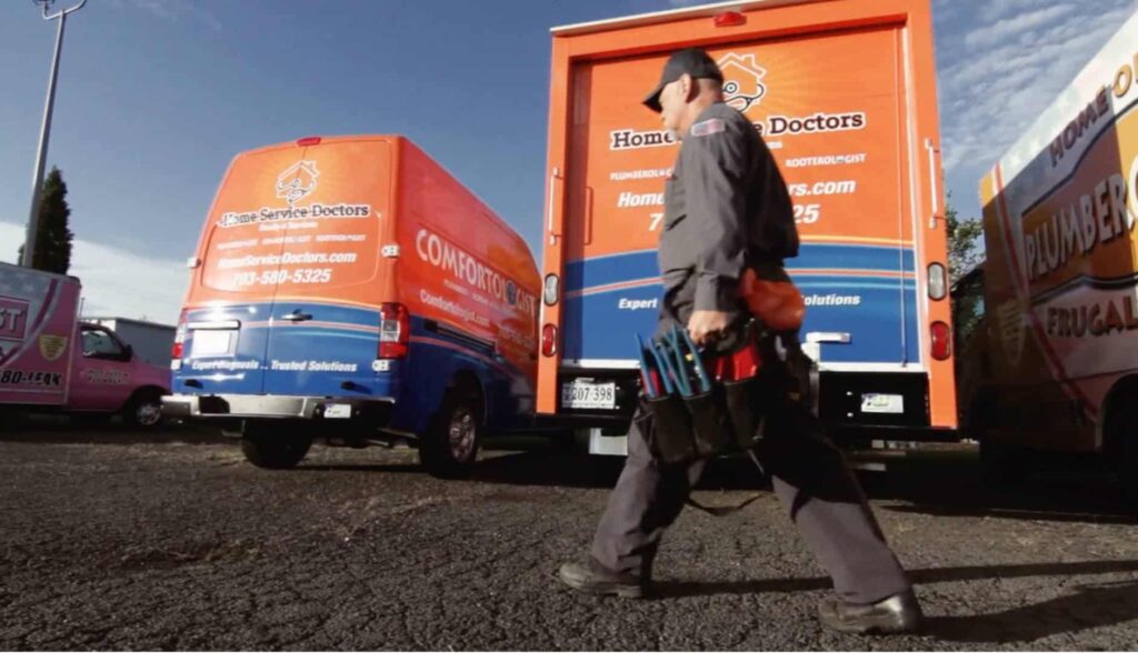 Home Service Doctors employee walking past work trucks in a parking lot.